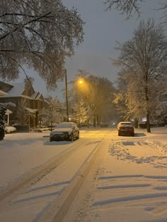 cars parked on the side of a snow covered road at night with street lights in the distance