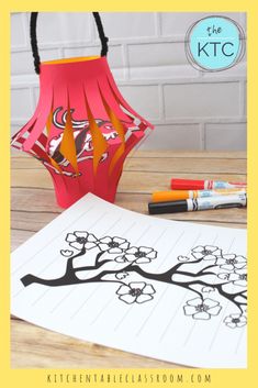 a paper lamp shade sitting on top of a wooden table next to markers and crayons