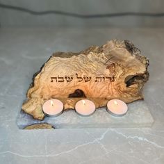 three lit candles sit in front of a piece of wood with an inscription on it