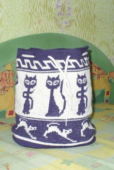 a blue and white knitted basket sitting on top of a green tablecloth covered bed