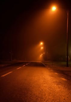 an empty road at night with street lights shining on it and fog in the air