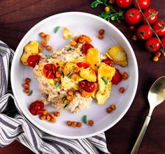 a white plate topped with rice and vegetables next to a silver spoon on top of a wooden table