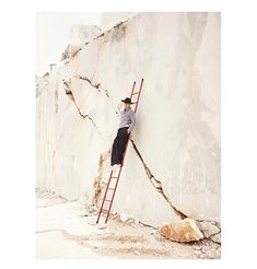 a man climbing up the side of a large rock with a ladder in his hand