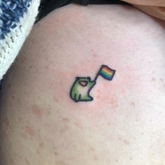 a small tattoo on the back of a woman's thigh with a green apple holding a rainbow flag