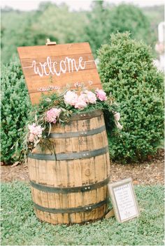 a welcome sign is placed on top of a wooden barrel with flowers and greenery