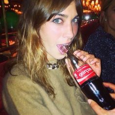 a young woman is taking a bite out of a coca - cola bottle while sitting in a restaurant