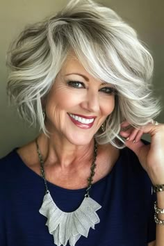 Smiling woman with short, wavy gray hair, wearing a blue top and a statement necklace. Shoulder Length Brown And Blonde Hair, Short Hairstyles For Square Face Over 50, Shaggy Haircuts Medium, Over 60 Hairstyles For Women, White Hair Highlights, Salt Pepper Hair, 70 Hair, Grey Hair Over 50, 60 Hairstyles