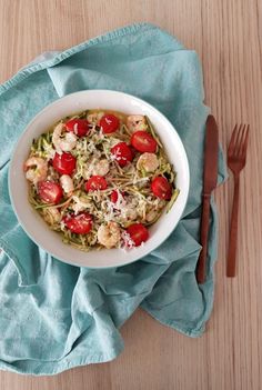 a white bowl filled with pasta and tomatoes on top of a blue napkin next to a fork