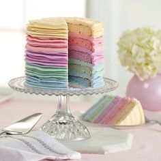 a multi - colored cake is on a glass plate with silverware and flowers in the background