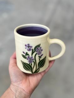 a hand holding a coffee cup with purple flowers on the outside and green leaves on the inside