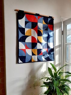 a potted plant sitting in front of a window next to a wall hanging quilt