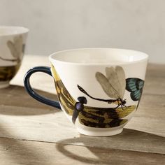 two mugs with dragonflies on them sitting on a table next to each other