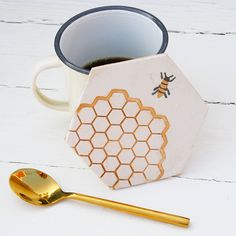 a cup of coffee next to a gold spoon and honeycomb coaster on a white table