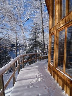 a snow covered walkway leading to a wooden cabin with large windows and trees in the background