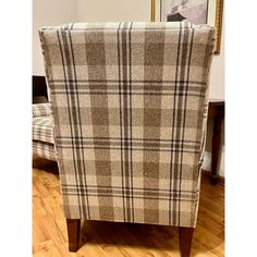 a plaid chair sitting on top of a hard wood floor next to a framed painting