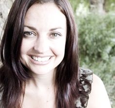 a woman with long brown hair smiling at the camera while standing next to a tree