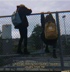 two people with backpacks standing next to each other behind a chain link fence that says i don't go looking for trouble trouble, usually finds me