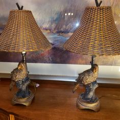 two lamps sitting on top of a wooden table next to a wall with a painting