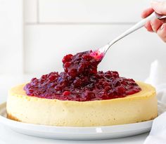 a person is spooning cranberry sauce onto a cheesecake on a plate