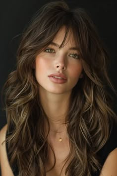 Portrait of a woman with tousled brunette hair and bangs, showcasing subtle makeup against a dark background. Haircuts For Long Hair Heart Shaped Face, Long Thick Layers, Curtain Bangs And Layers Brown Hair, Curtain Bangs With Long Layered Hair, Wavy Long Curtain Bangs, Medium Hair Length With Curtain Bangs, Bardot Bangs Wavy Hair, Long Wavy Hair With Layers And Curtain Bangs, Middle Part Long Bangs