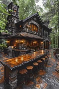 an outdoor bar with stools and tables in front of a stone building surrounded by trees