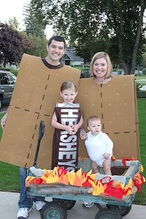 two adults and a child standing in front of a cardboard box with fire on it