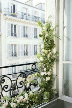 a balcony with flowers and vines on the railing, next to a window in an apartment building