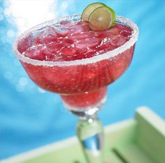 a close up of a drink in a wine glass with ice and lime on the rim