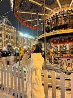 a woman is standing in front of a merry go round with lights on the carousel