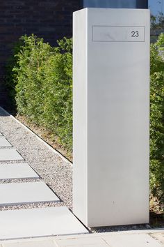 a tall white box sitting on top of a sidewalk next to a lush green bush