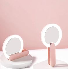 two round mirrors sitting next to each other on top of a white table with a pink wall in the background