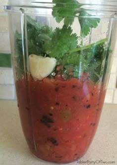 a blender filled with red sauce and garnished with cilantro leaves