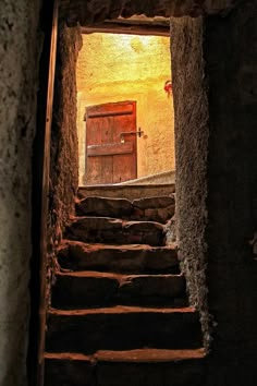 the stairs lead up to an open door in a stone building with light coming through