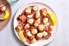 a white plate topped with bacon wrapped scallops next to a lemon wedge