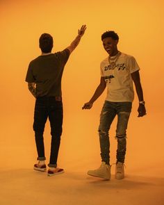 two young men standing next to each other in front of an orange background with one holding his hand up