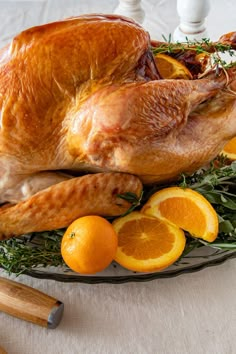 a roasted turkey on a platter with oranges and herbs