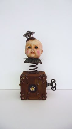 an old fashioned doll sitting on top of a box with a key in it's mouth