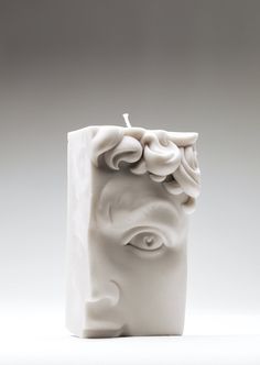 a white candle with a face on it and an eye in the middle, sitting against a gray background