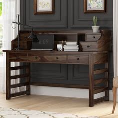 a wooden desk with drawers and a laptop on it in front of two framed pictures