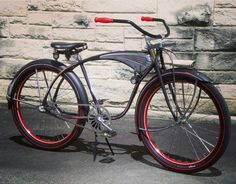 a bike with red rims parked in front of a brick wall on the street