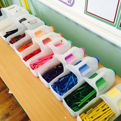 a wooden table topped with lots of plastic containers filled with different colored pencils and markers