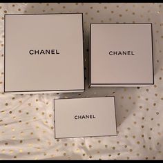 three chanel boxes sitting on top of a white tablecloth covered with gold dots