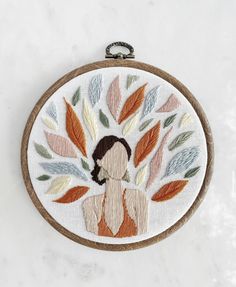 a woman's face is surrounded by leaves in an embroidered hoop on a marble surface