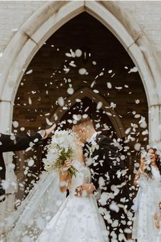 a bride and groom standing in front of an arch with white confetti falling from it