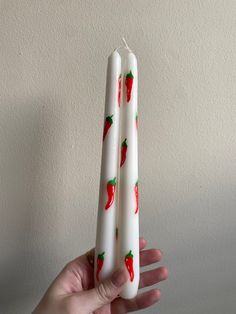 two white candles with red peppers painted on them are held in front of a wall