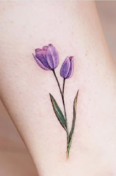 a small purple flower on the side of a woman's leg with green leaves