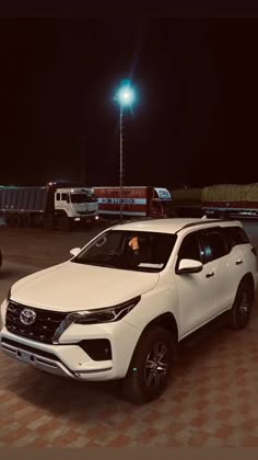 two white suvs are parked next to each other in the parking lot at night