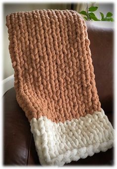 a brown and white blanket sitting on top of a leather couch next to a potted plant