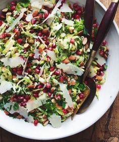 a white bowl filled with salad and two serving utensils on top of a wooden table