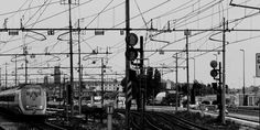 black and white photograph of trains on tracks in an industrial area with power lines overhead